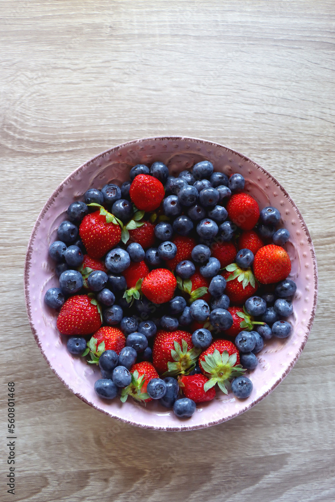 Pink rustic bowl filled with fresh blueberries and strawberries. Wooden background, top view. Pink rustic bowl filled with fresh blueberries and strawberries. Wooden background, top view.