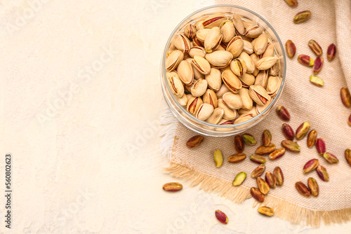 Bowl with nuts, scattered pistachio kernels and napkin on beige background