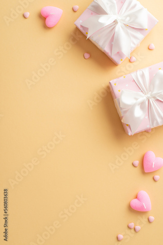 Valentine's Day concept. Top view vertical photo of pink gift boxes with white ribbon bows heart shaped candles and sprinkles on isolated pastel beige background with empty space