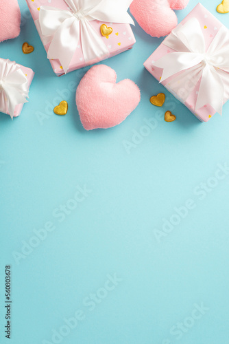 Valentine's Day concept. Top view vertical photo of pink present boxes with satin ribbon bows heart shaped fluffy toys golden hearts and sprinkles on isolated pastel blue background with blank space