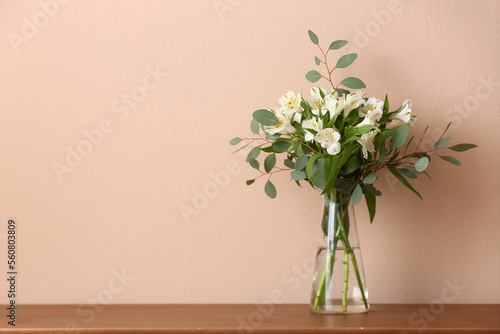 Vase with bouquet of beautiful alstroemeria flowers and eucalyptus branches on table near color wall photo