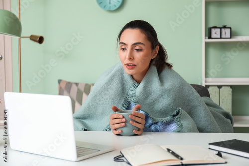 Frozen young woman with cup of tea working at home