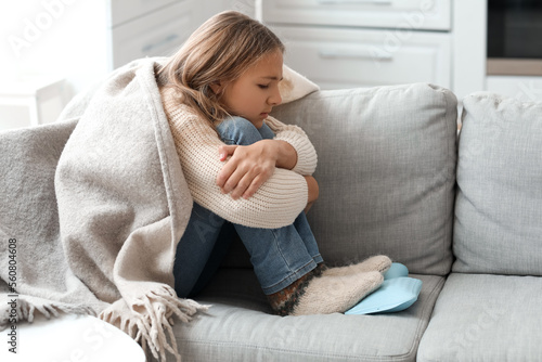 Fotografia Ill girl warming her feet with hot water bottle on sofa at home