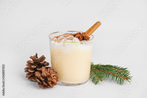Glass of tasty eggnog cocktail, fir branch and cones on white background photo