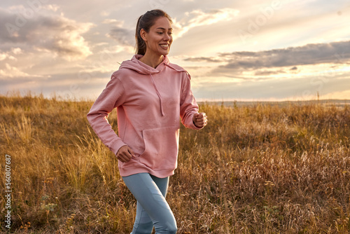 Woman in sportswear running in field at sunrise. Active rest on weekends. Traveling in nature. Caucasian european female enjoy sport  fitness outdoors. motivated healthy lady in the morning
