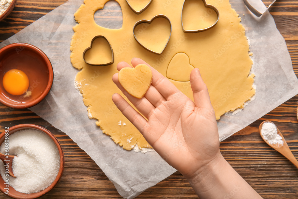Female hand with raw cookie, dough and cutters on wooden background, closeup. Valentines Day celebration Female hand with raw cookie, dough and cutters on wooden background, closeup. Valentines Day celebration