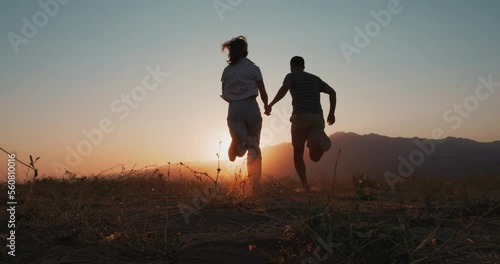 Back view of love couple silhouette running into the sunset. Happy young man and woman running holding hands, in nature 4k slowmotion