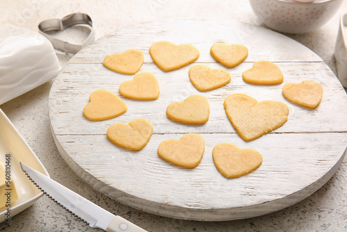 Wooden board with raw heart shaped cookies on light table, closeup. Valentines Day celebration