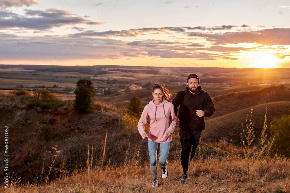 Athletic strong couple running jogging together at sunset, in nature mountains hills. focused man and woman run along the field. motivation and endurance, wellness, lifestyle concept