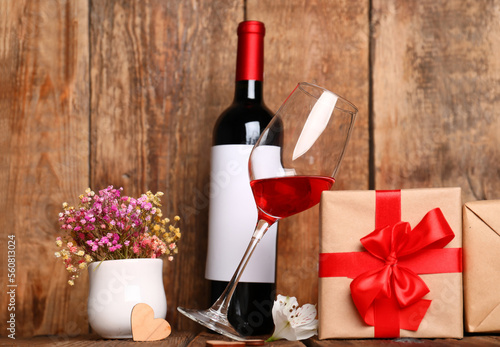 Glass of wine, gift for Valentines Day and flowers on wooden background