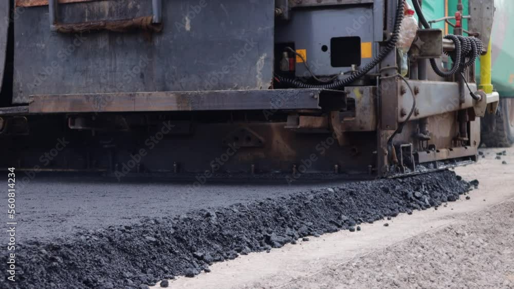 Repair and construction of the road, paver compresses the asphalt. Heavy special equipment and hot asphalt concrete close-up. Asphalt paver in operation, bottom view. Repair and construction of the road, paver compresses the asphalt. Heavy special equipment and hot asphalt concrete close-up. Asphalt paver in operation, bottom view.