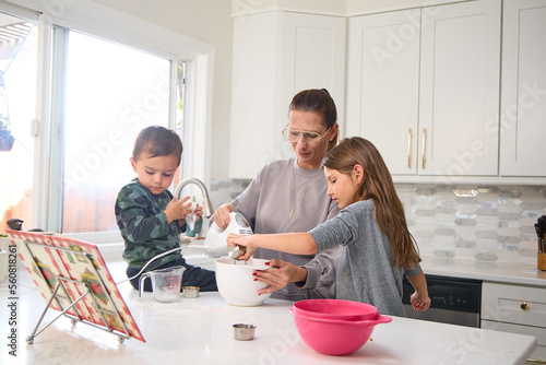 A mother is baking in the kitchen with her young son and daughter