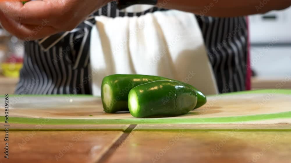 Woman cutting jalapeno pepper in kitchen