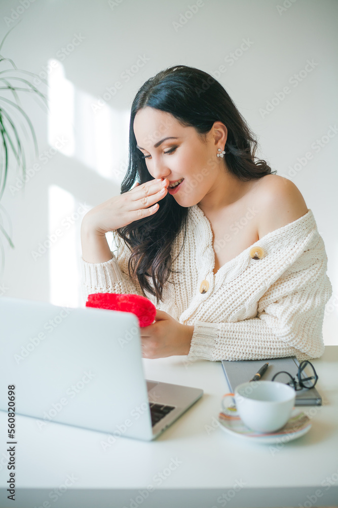 Young beautiful dark-haired woman of 34 years old in knitted sweater is talking on videophone and holding plush heart in her hands. Valentine's Day. Model received gift. Young beautiful dark-haired woman of 34 years old in knitted sweater is talking on videophone and holding plush heart in her hands. Valentine's Day. Model received gift.