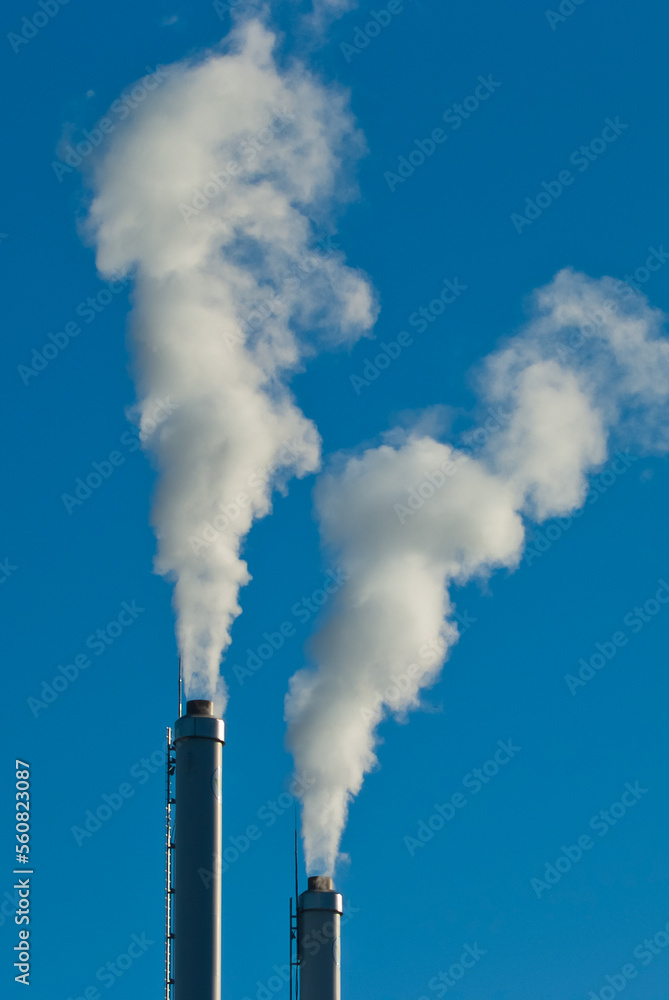 factory chimneys and white smoke against a blue sky