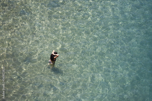 Aerial view to azure sea and woman going to swim in transparent water. Sunny holidays, beach vacation