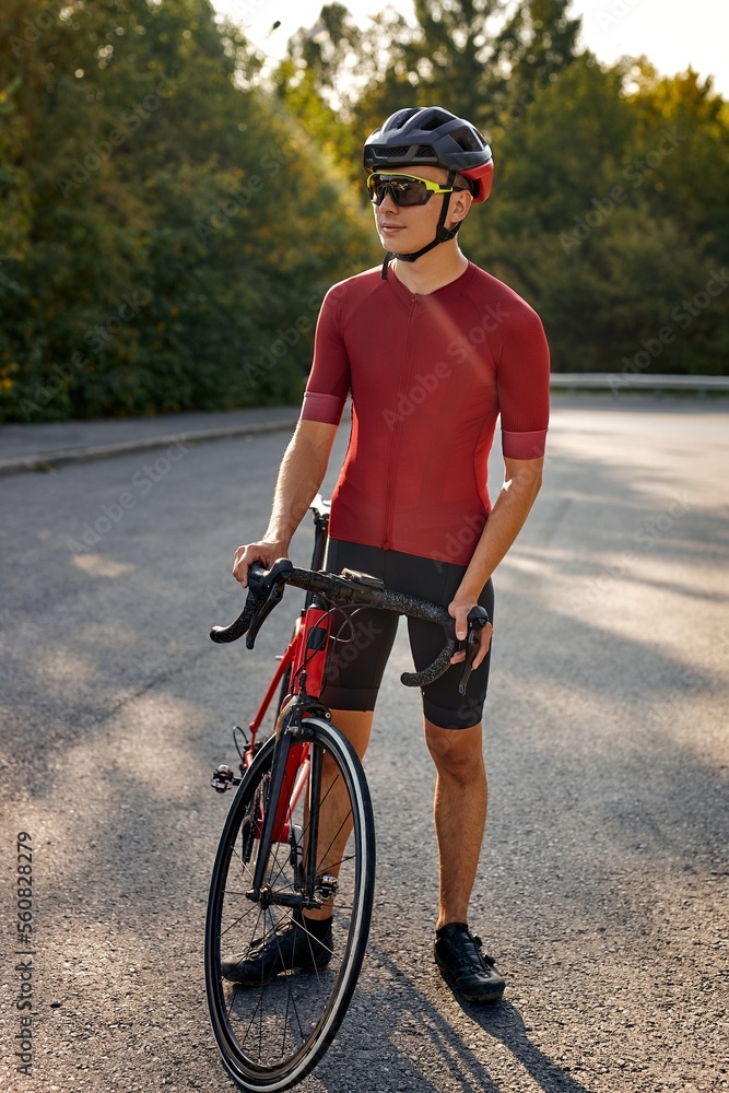 Obraz premium handsome man with athletic body shape in protective helmet and glasses have rest during riding bicycle with beautiful nature around. Concept of sport, self discipline and motivation.