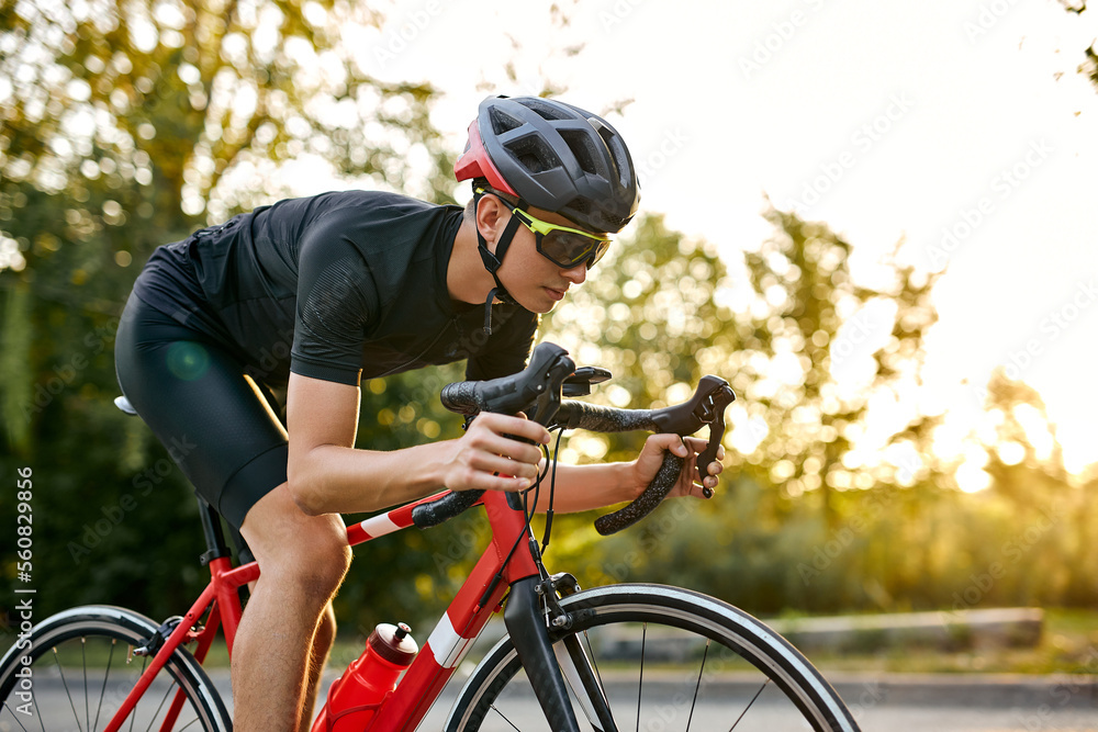 strong athlete man in sport clothing and helmet riding professional bike on nature. confident young caucasian sportsman enjoying favorite hobby on paved road. at summer season, sunset strong athlete man in sport clothing and helmet riding professional bike on nature. confident young caucasian sportsman enjoying favorite hobby on paved road. at summer season, sunset
