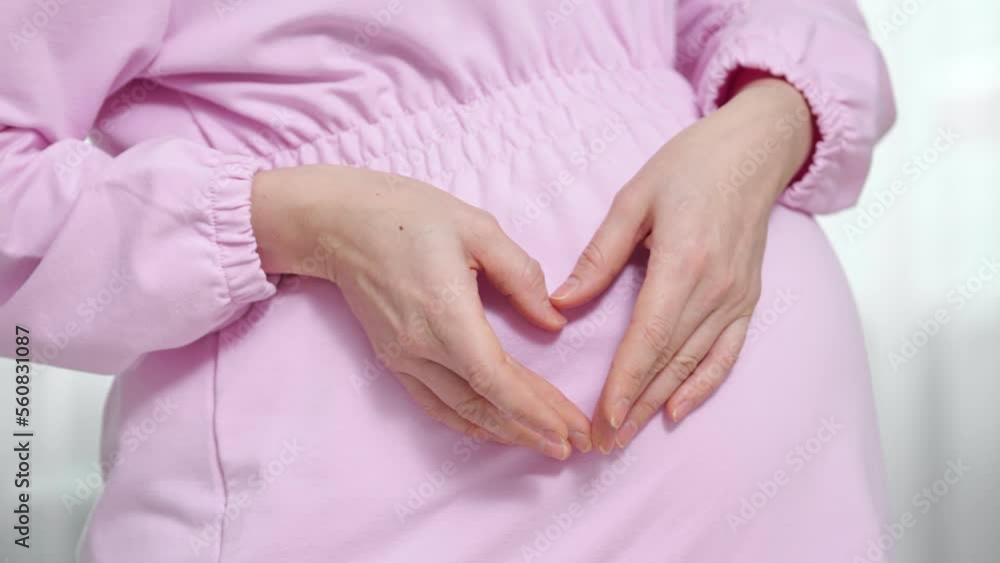 Pregnant woman shows fingers heart near big bump with upcoming baby and wants to become nice mother. Lady awaits for child and expects to give birth Pregnant woman shows fingers heart near big bump with upcoming baby and wants to become nice mother. Lady awaits for child and expects to give birth