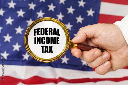 In front of the American flag, a man holds a magnifying glass in his hand with the inscription - federal income tax photo