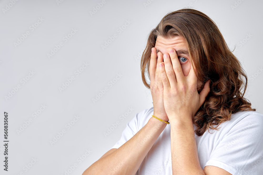 Portrait of shocked surprised male looking at camera through one eye. Young caucasian male in casual wear is emotionally reacts on something, in fear, frightened or shocked by something Portrait of shocked surprised male looking at camera through one eye. Young caucasian male in casual wear is emotionally reacts on something, in fear, frightened or shocked by something