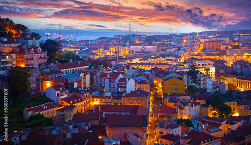Lisbon, Portugal. Top view panorama of sunset. Evening picturesque scene at houses in historic old town district Alfama. 25th April Bridge far away. Sky with dramatic clouds