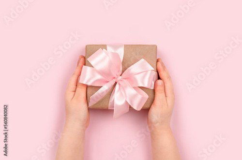 Girl's hands holding gift box with pink ribbon on pastel pink background