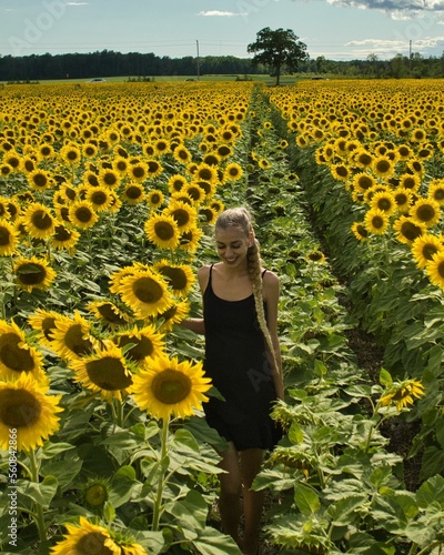 Young women walking though a field of endless sunflowers on a cloudy day