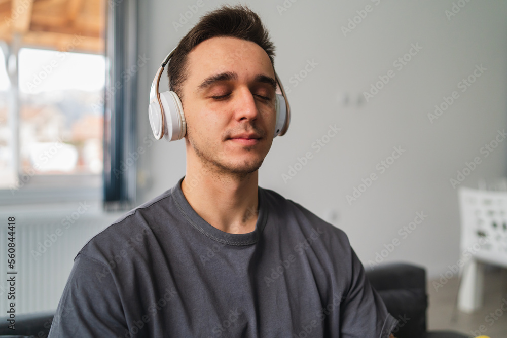 A young guy is sitting on couch meditating and stretching while listening to music and using his mobile phone in his house during the day A young guy is sitting on couch meditating and stretching while listening to music and using his mobile phone in his house during the day