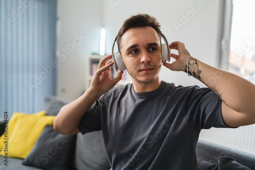 A young guy is sitting on couch meditating and stretching while listening to music and using his mobile phone in his house during the day