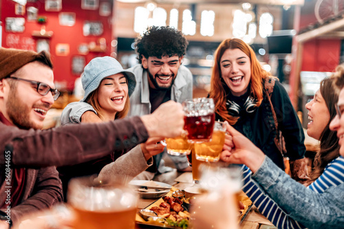 Group of happy friends drinking and toasting beer at brewery bar restaurant - Young people eating bbq at pub - Friendship concept with young people having fun together - Focus on chicken wing