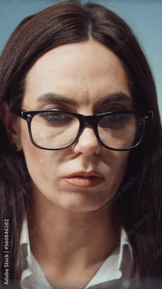 Vertical Screen: Pensive woman with long hair wearing eyeglasses working in office. Closeup portrait of businesswoman winking while reading documents or typing on laptop. Concept of occupation Vertical Screen: Pensive woman with long hair wearing eyeglasses working in office. Closeup portrait of businesswoman winking while reading documents or typing on laptop. Concept of occupation