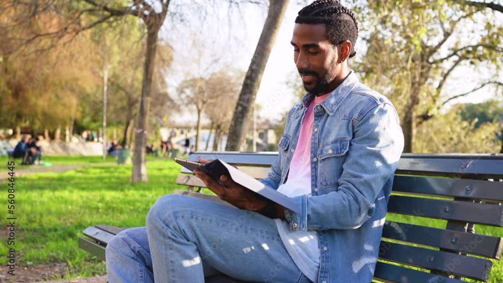 Young man sitting on a bench in the park, taking and using a digital tablet to read the news Young man sitting on a bench in the park, taking and using a digital tablet to read the news