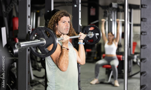 Caucasian man training with barbell using squat rack in gym