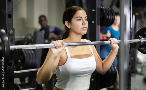 Caucasian woman doing exercises usining barbell and half rack in gym