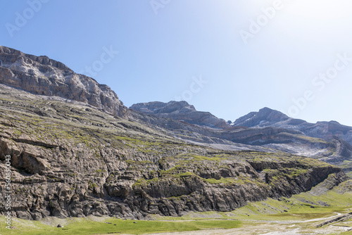 Green landscape in the pyrenees with layered mountains, green meadow and flowers, blue sky with clouds and path