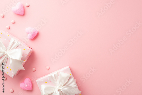 Valentine's Day concept. Top view photo of trendy gift boxes with satin ribbon bows heart shaped candles and sprinkles on isolated pastel pink background with copyspace