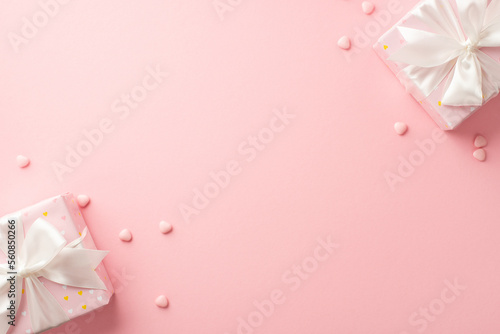 St Valentine's Day concept. Top view photo of stylish present boxes with white ribbon bows and heart shaped sprinkles on isolated pastel pink background with blank space © ActionGP