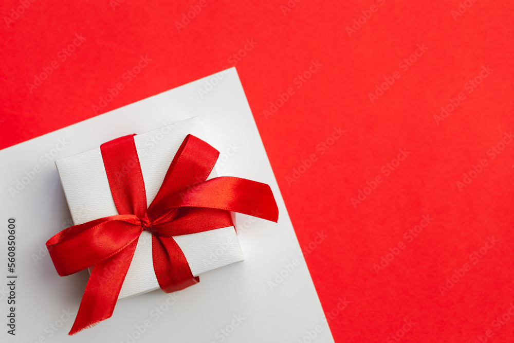 Gift box with a red bow on a red background, flat lay, Valentine's day concept, festive minimalistic background, copy space.