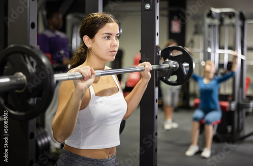 Caucasian woman training with barbell using squat rack in gym