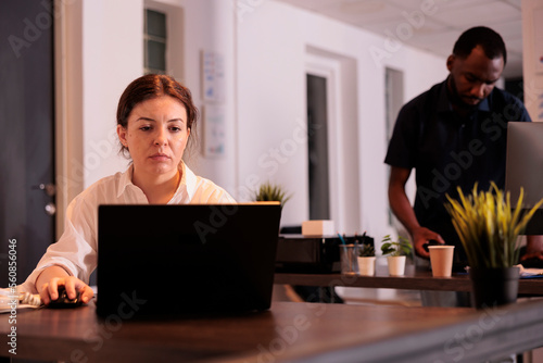 Tired corporate employee working on laptop in office late, project manager typing on computer. Worker analyzing company report, woman in modern coworking space with warm light