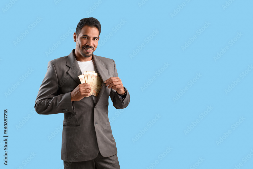 Businessman putting money in his suit pocket on a cyan background. looking at the camera Businessman putting money in his suit pocket on a cyan background. looking at the camera
