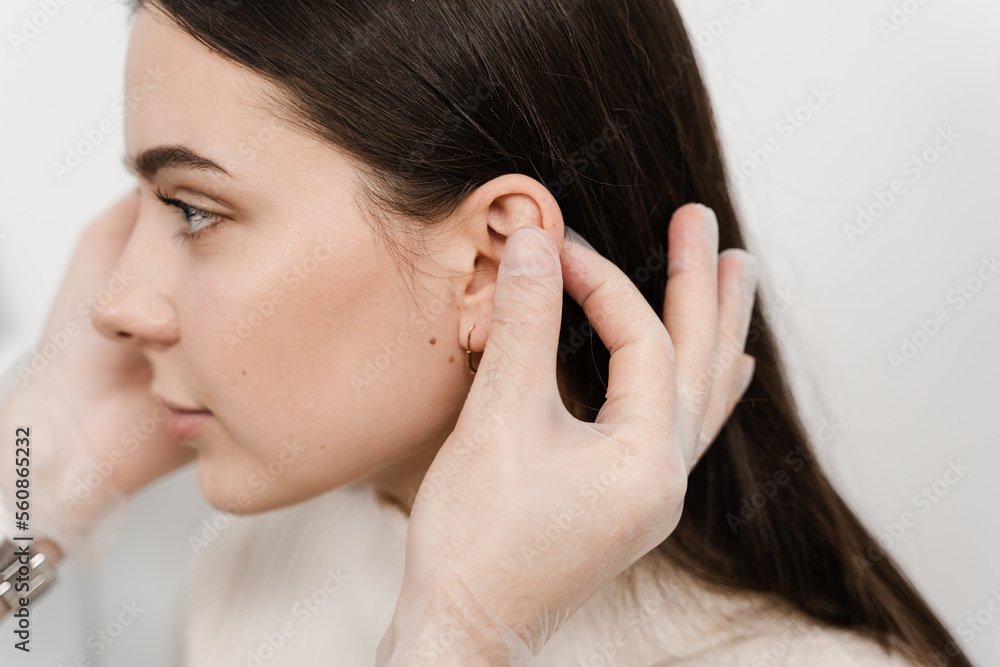 Otoplasty ear surgery. Surgeon doctor examines girl ears before otoplasty cosmetic surgery. Otoplasty surgical reshaping of pinna and ear. Otoplasty ear surgery. Surgeon doctor examines girl ears before otoplasty cosmetic surgery. Otoplasty surgical reshaping of pinna and ear.