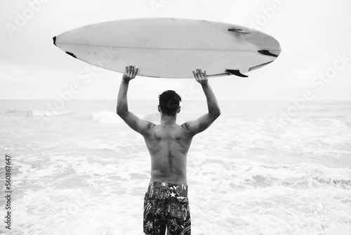 Male surfer holds surfboard up and looks at the ocean. photo