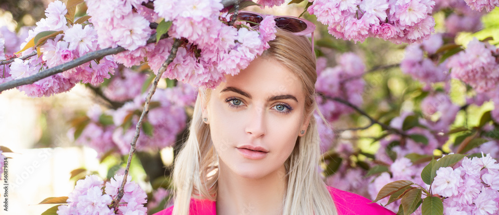 Fototapeta premium Sensual woman near sakura tree background, banner for website header. Spring girl. Outdoor portrait of young beautiful happy smiling female model near flowering tree.