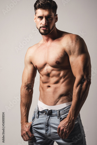 Male model with perfect body in jeans posing over grey background. Close-up. Studio shot.