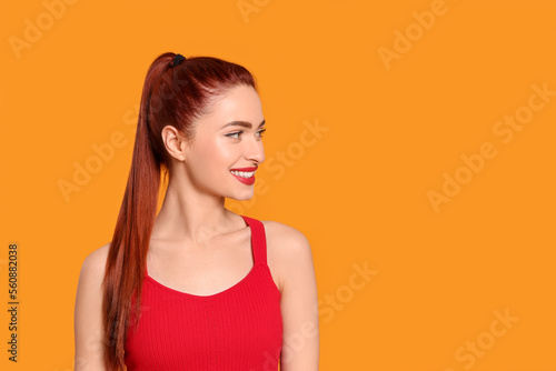 Happy woman with red dyed hair on orange background, space for text