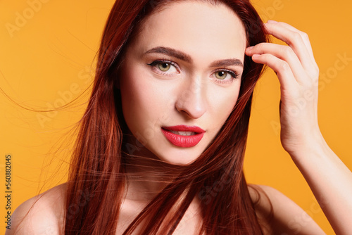 Beautiful woman with red dyed hair on orange background