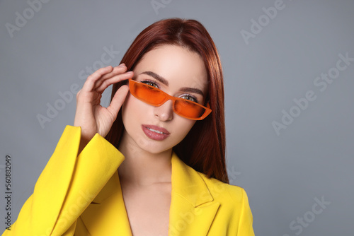 Stylish woman with red dyed hair and orange sunglasses on light gray background © New Africa