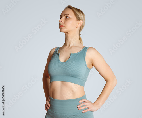 A young blonde girl in yoga clothes stands in a hero pose. Proud strong woman in sportswear